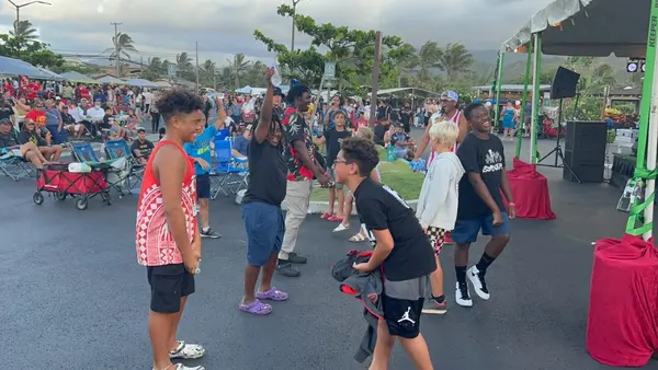 A community gathering outdoors with youth and adults near a stage during an event